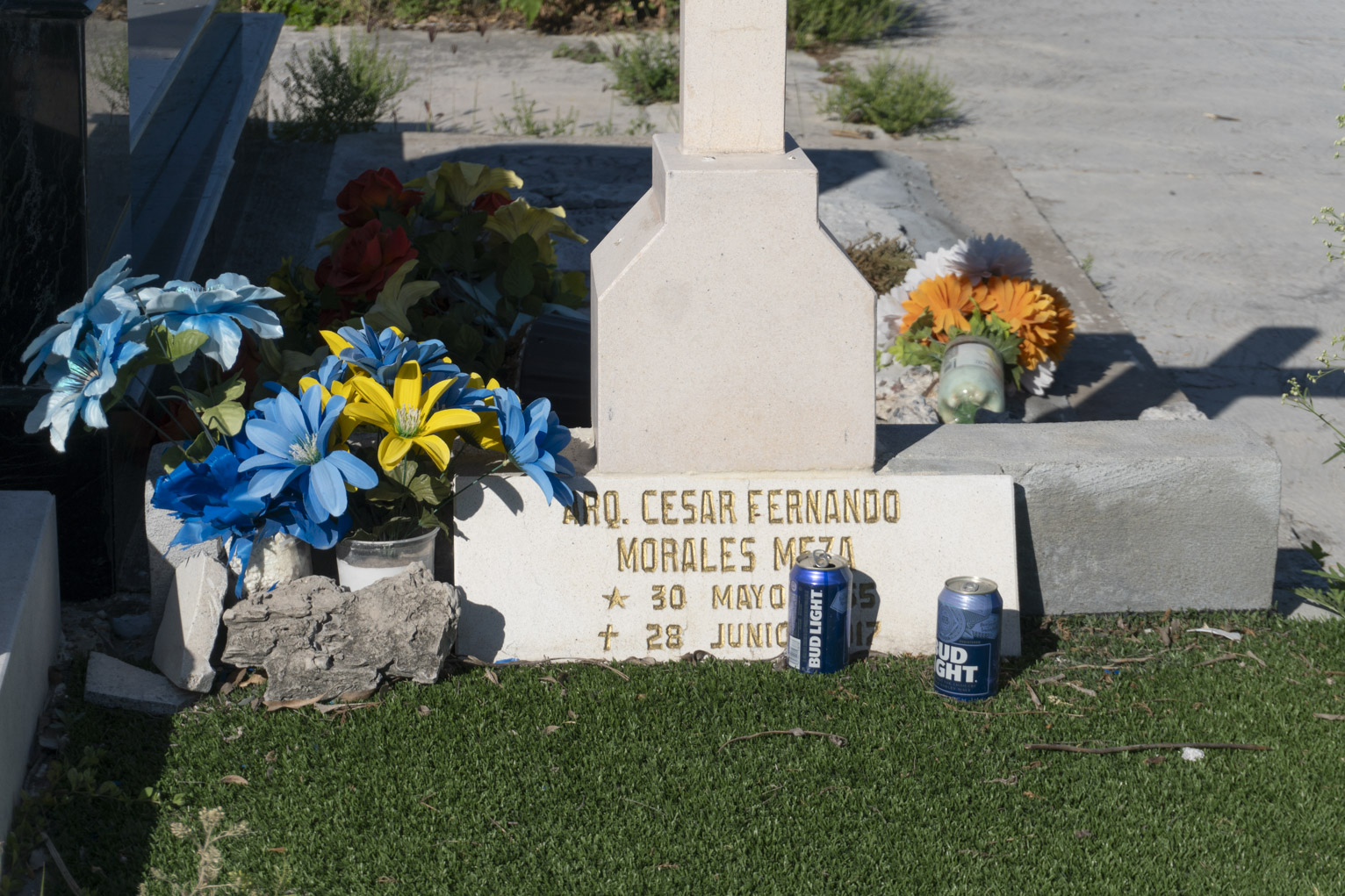 A grave marker with flowers and two cans of beer